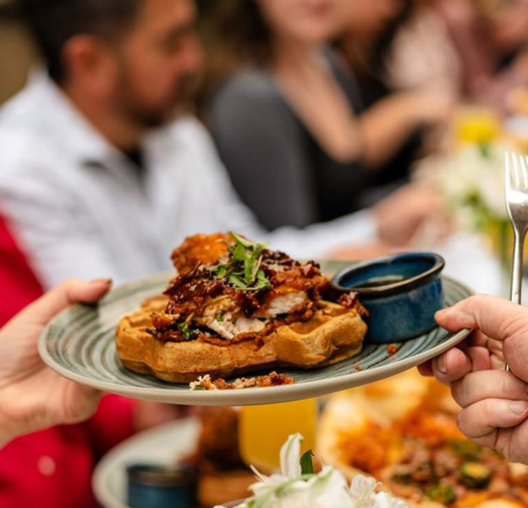Hands passing eachother a plate of gourmet waffles.