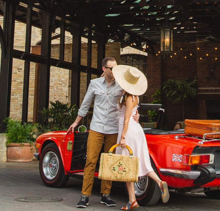 Woman in large hat and man embracing in front of Hotel Emma in San Antonio.