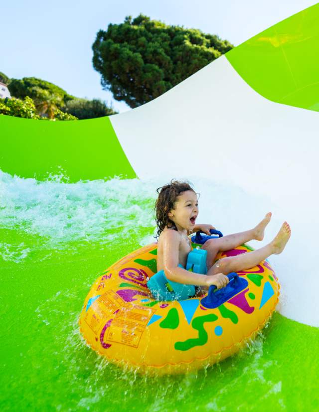 Child on inner tube on waterslide laughing.
