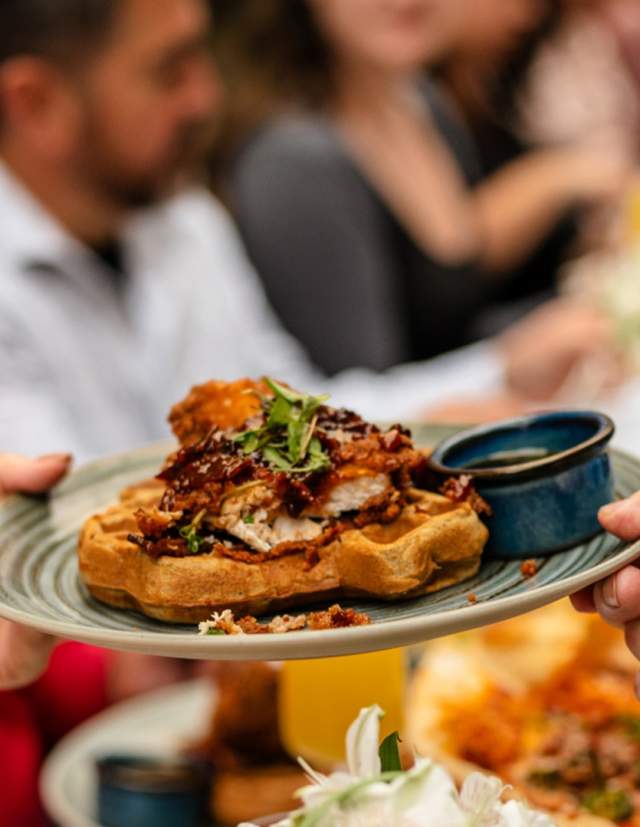 Hands passing eachother a plate of gourmet waffles.