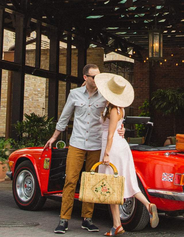 Woman in large hat and man embracing in front of Hotel Emma in San Antonio.