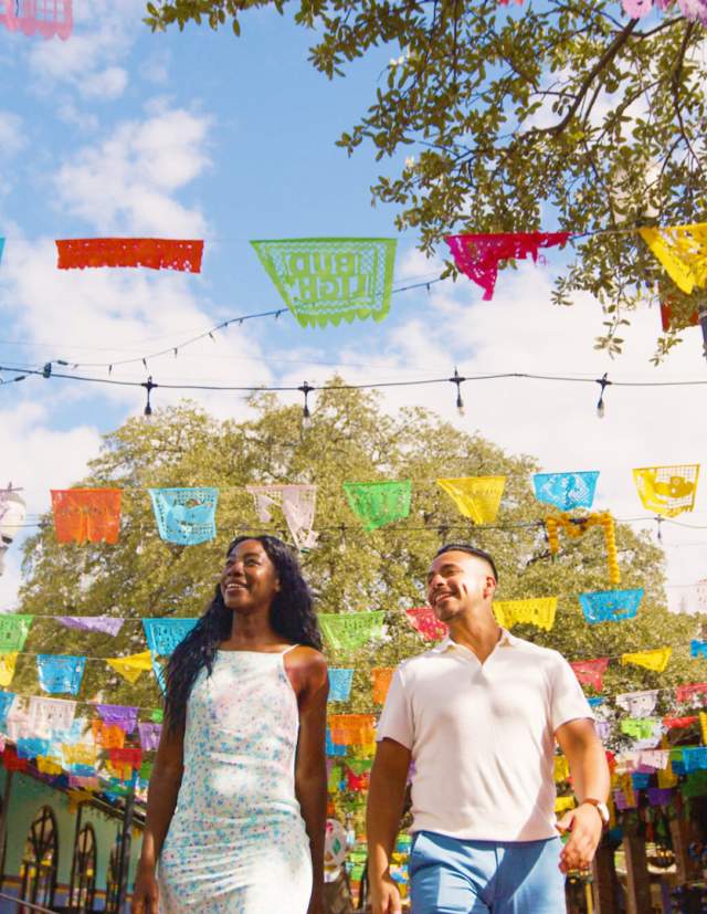 Couple walking through Historic Market Square with papel picado above them