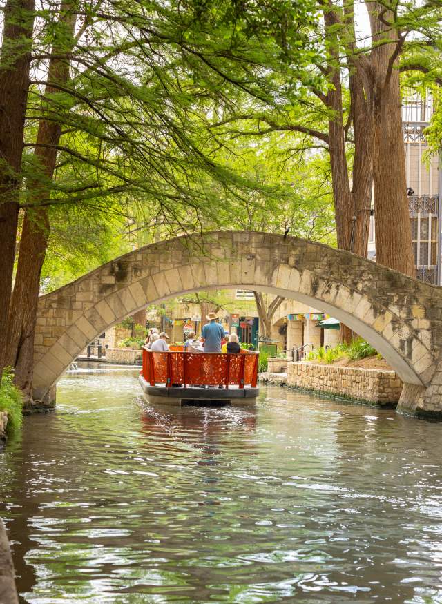 Red GO RIO River barge floating under bridge on San Antonio River Walk.