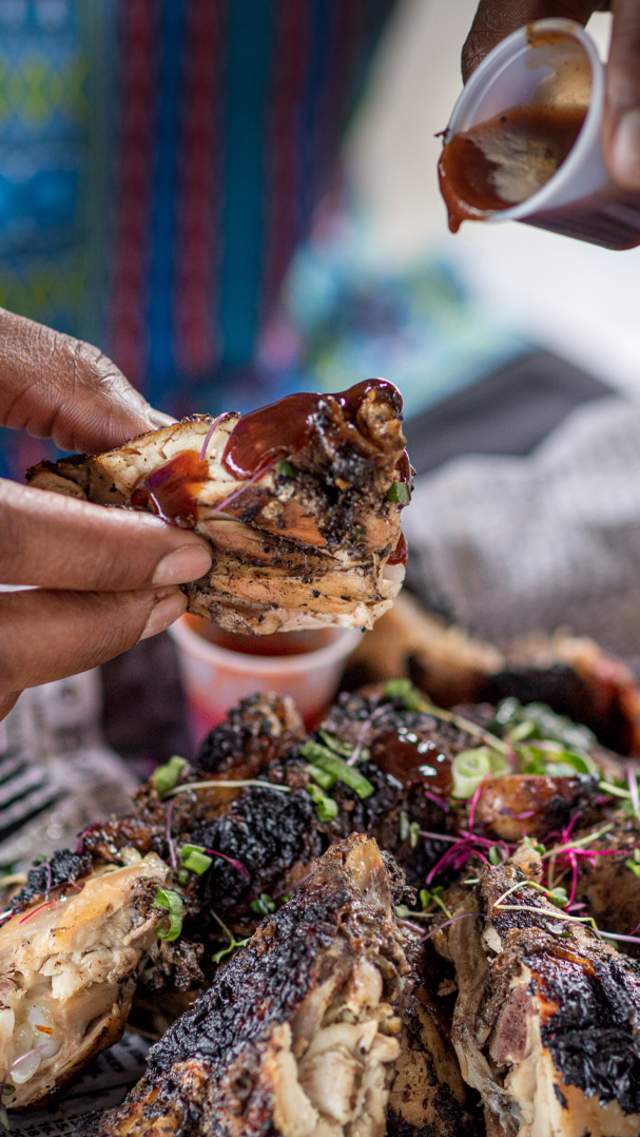 Hands dipping Jerk Chicken into barbecue sauce at The Jerk Shack.