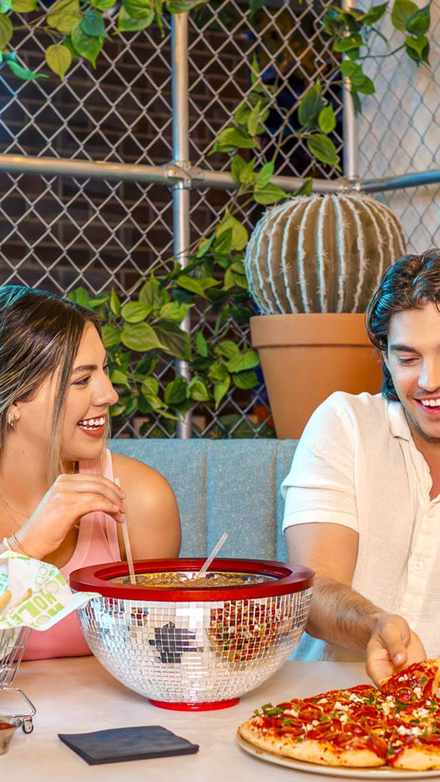 Boy and girl at table laughing, eating pizza, and enjoying drinks.