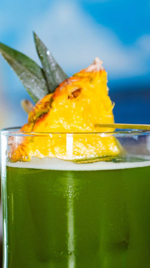 Green cocktail drink with pineapple on top.