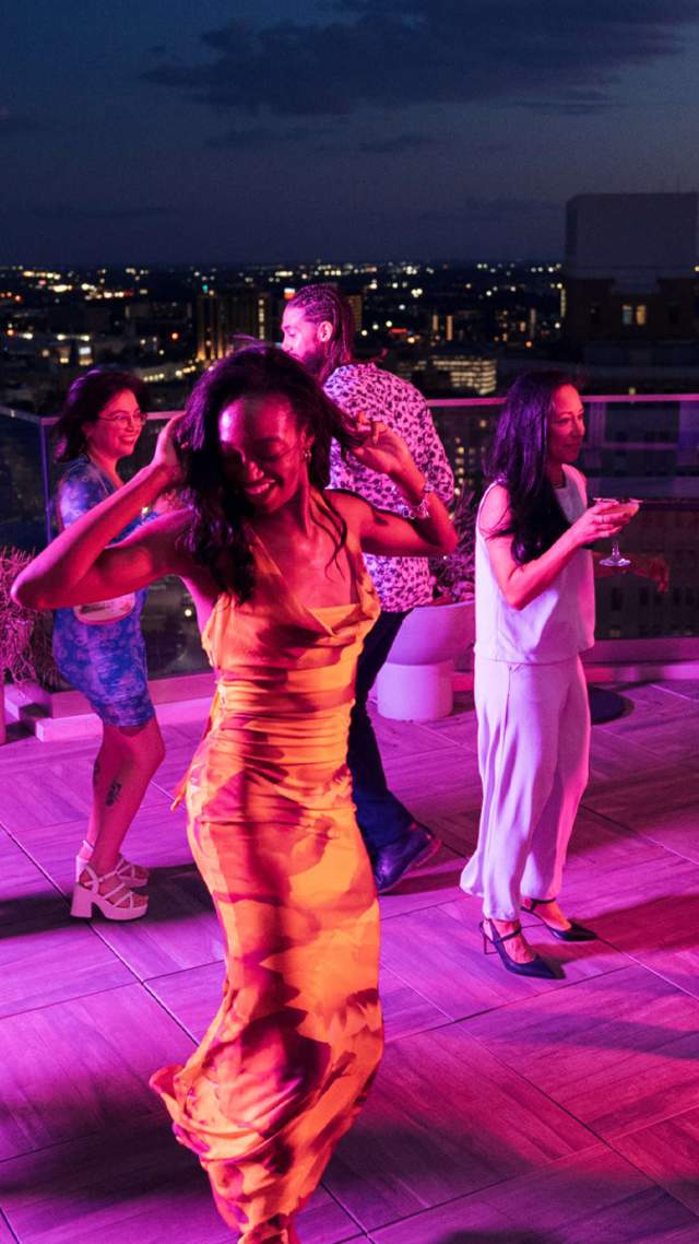 Crowd dancing around woman at rooftop bar in San Antonio.
