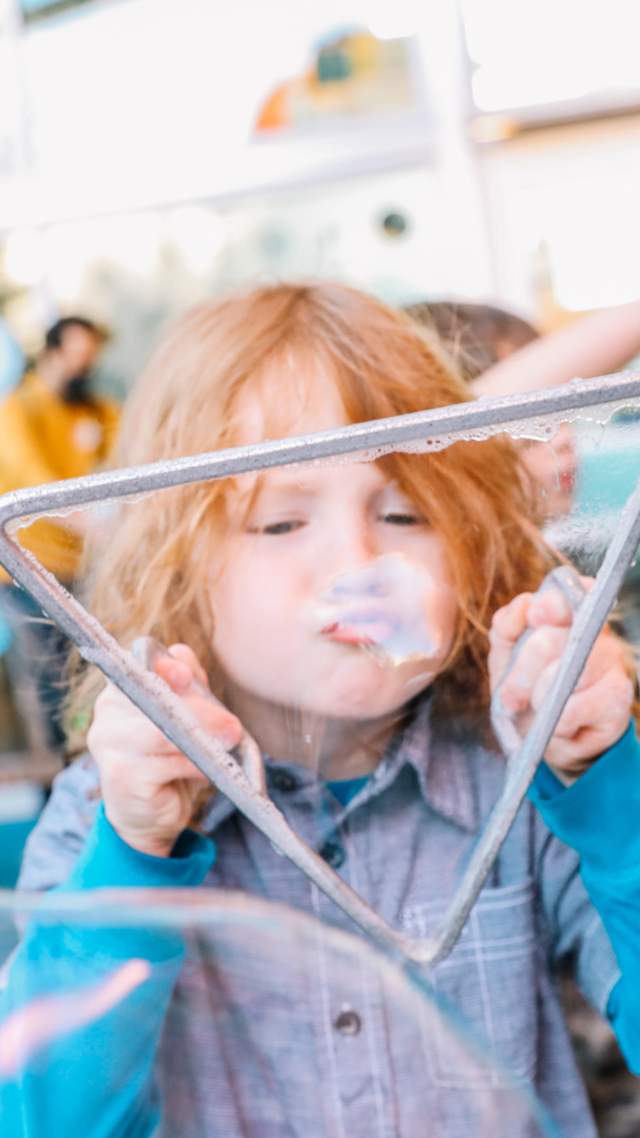 Child blowing bubble through triangular bubble-blower.