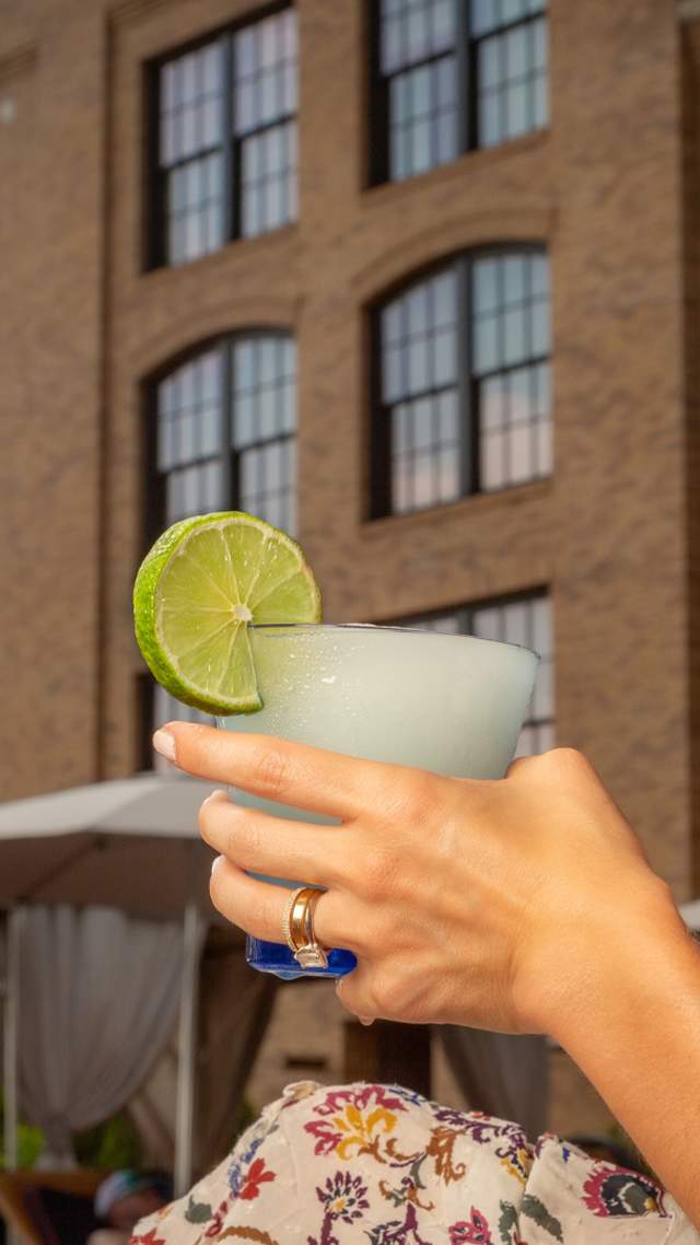 Woman holding glass with cool drink and lime and Hotel Emma in the background.