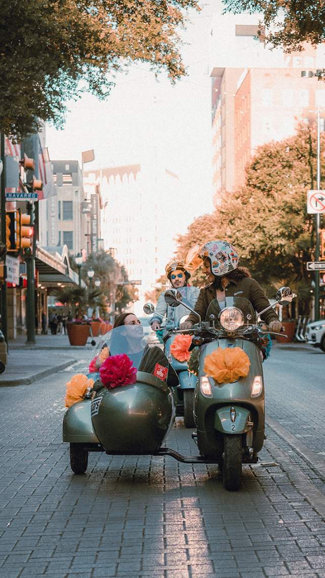 Woman driving vespa with passenger in side car in San Antonio, Texas.