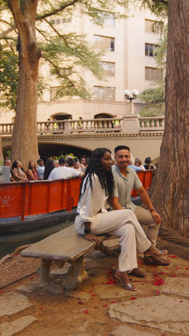 Couple sitting on bench at the River Walk in front of Go Rio RIver Cruise barge