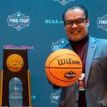 Man holding basketball by NCAA trophy