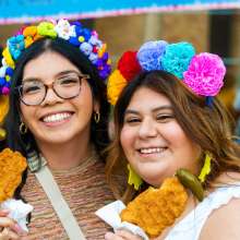 Two girls holding chicken on a stick wearing flower crows at Fiesta San Antonio.