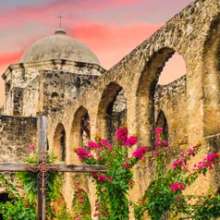 Wooden cross at San Antonio Missions National Historical Park with pink sky in background.