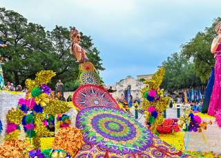 Parade participants on float dressed in elaborate dresses at Battle of Flowers parade in San Antonio in Fiesta San Antonio.