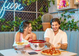 Boy and girl at table laughing, eating pizza, and enjoying drinks.