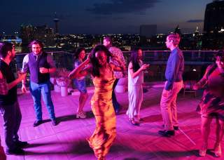 Crowd dancing around woman at rooftop bar in San Antonio.