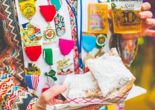 Person holding pastries in powdered sugar wearing Fiesta medals