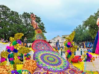 Parade participants on float dressed in elaborate dresses at Battle of Flowers parade in San Antonio in Fiesta San Antonio.