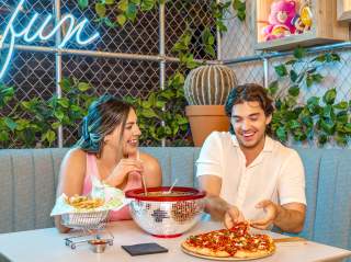 Boy and girl at table laughing, eating pizza, and enjoying drinks.