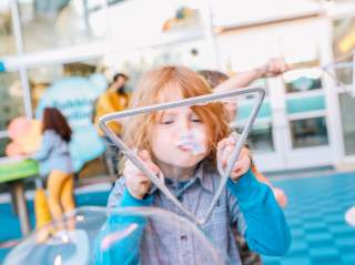 Child blowing bubble through triangular bubble-blower.