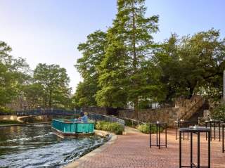 River barge floating along River Walk with large trees in background