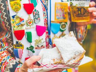 Person holding pastries in powdered sugar wearing Fiesta medals