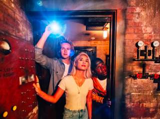 Girl and two boys opening door and holding flashlight.
