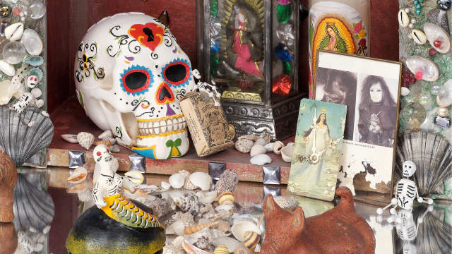 Art piece featuring altar components like sugar skulls, photos, and candles