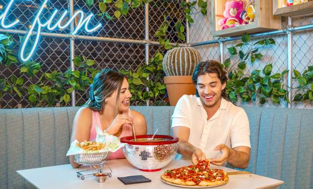 Boy and girl at table laughing, eating pizza, and enjoying drinks.