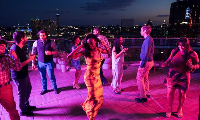 Crowd dancing around woman at rooftop bar in San Antonio.