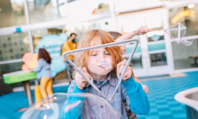 Child blowing bubble through triangular bubble-blower.