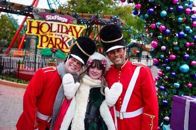 guest posing in front of holiday in the park signage at six flags