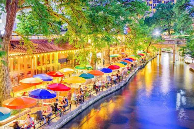 Colorful umbrellas lit up along the River Walk at dusk.