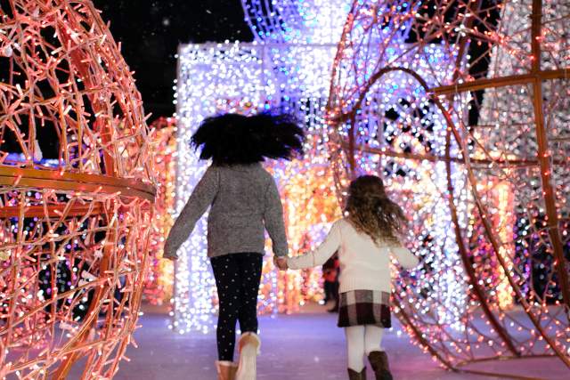 Two girls running toward large holiday light displays.