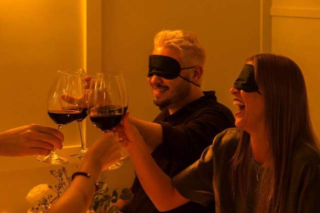 couple cheersing wine with blindfolds at dining in the dark