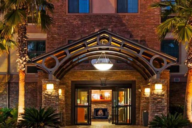 Exterior view of hotel entrance with palm trees on both sides of doors.