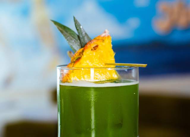 Green cocktail drink with pineapple on top.