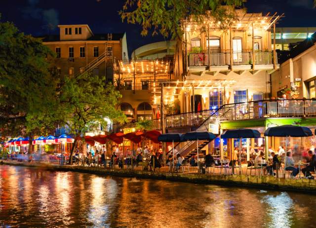 Restaurants along the River Walk in San Antonio at night with lights reflecting off the water.