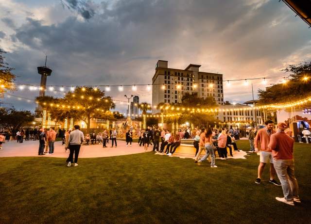 Large outdoor gathering at dusk with decorative lighting