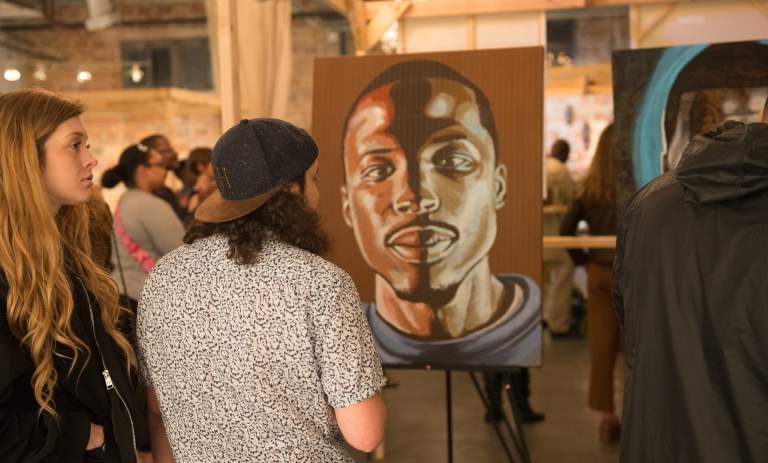 Man and woman viewing portait of a man at a gallery at DreamWeek San Antonio.