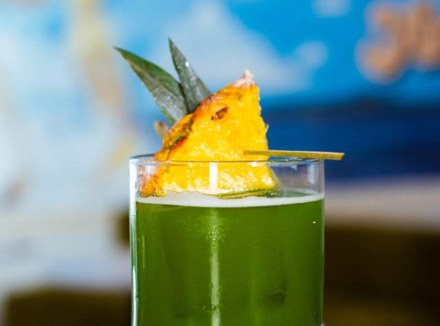 Green cocktail drink with pineapple on top.