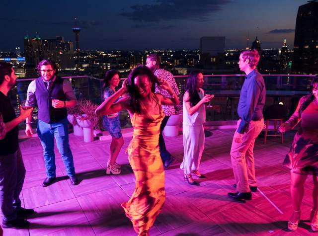 Crowd dancing around woman at rooftop bar in San Antonio.