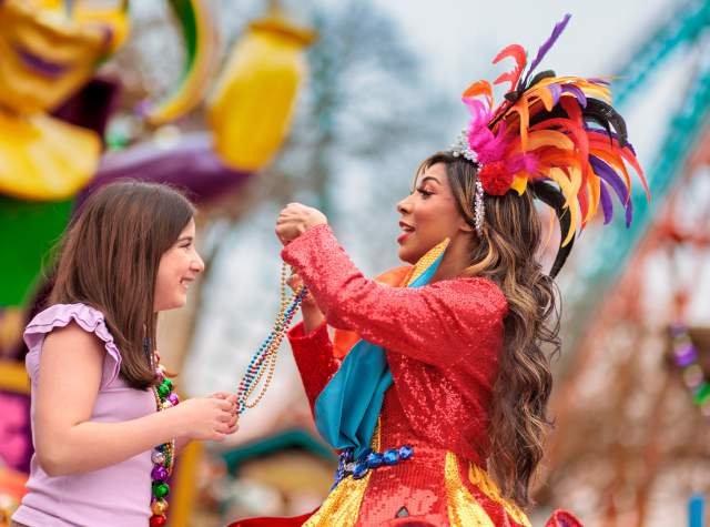 Costumed performer placing beads over girl's head at Six Flags Fiesta Texas' Mardi Gras Festival.