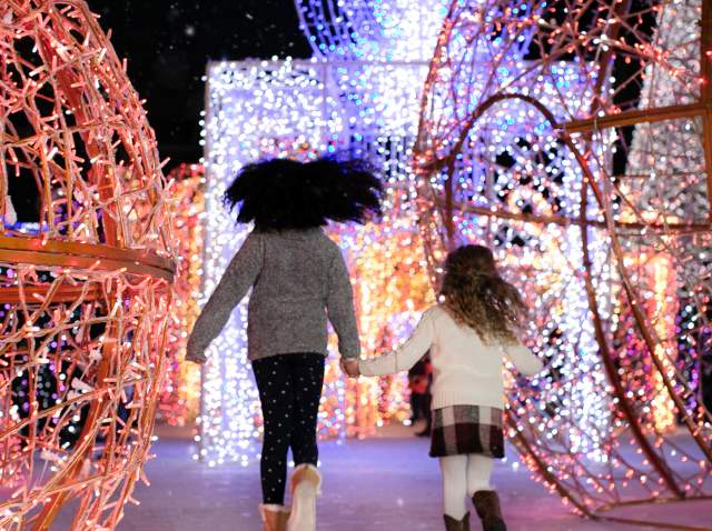 Two girls running toward large holiday light displays.