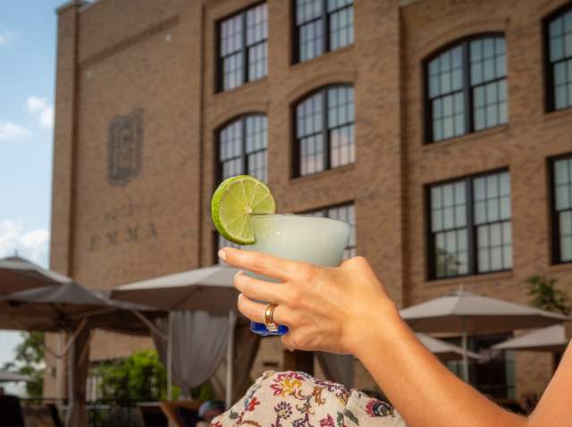 Woman holding glass with cool drink and lime and Hotel Emma in the background.
