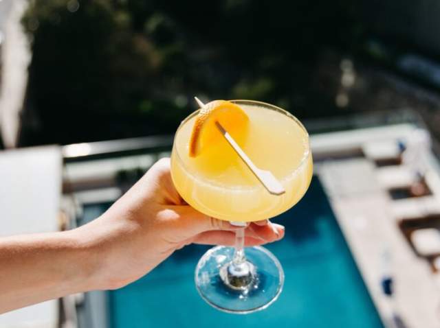 Person holding drink with blue pool in the background