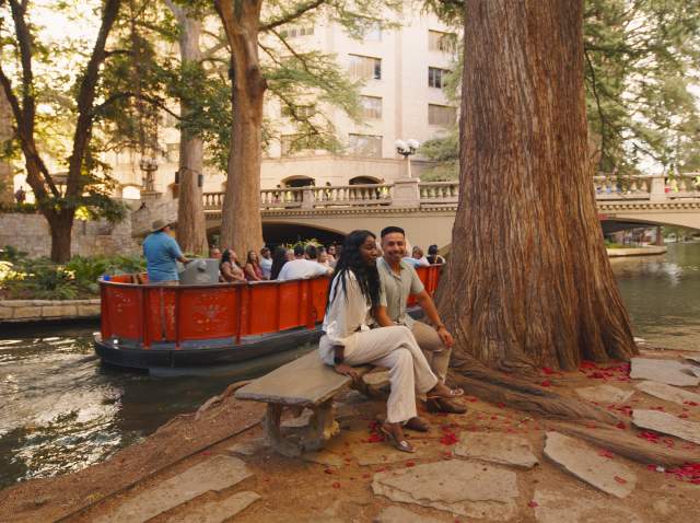 Couple sitting on bench at the River Walk in front of Go Rio RIver Cruise barge