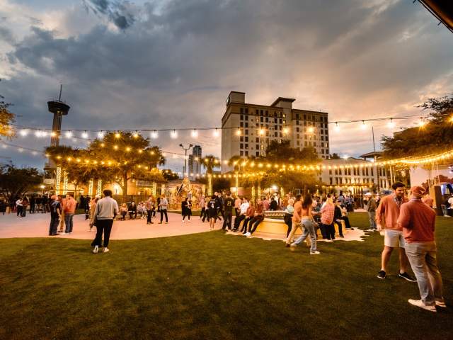 Large outdoor gathering at dusk with decorative lighting