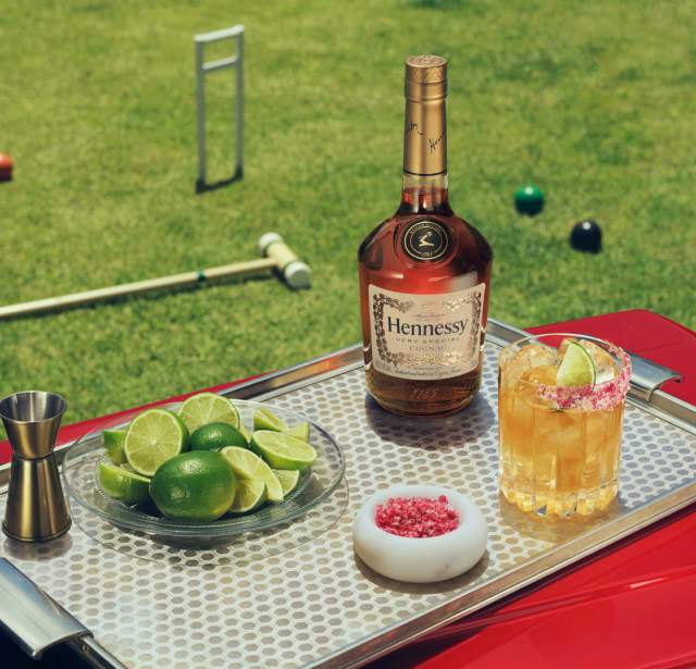 Table with Hennessy bottle and cocktail and croquet game in the background.